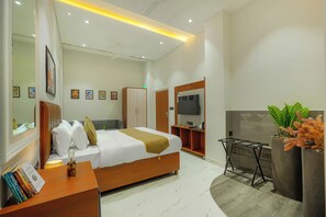 Un dormitorio moderno con cama, mesita de noche, libros, televisor, armario y una planta.
