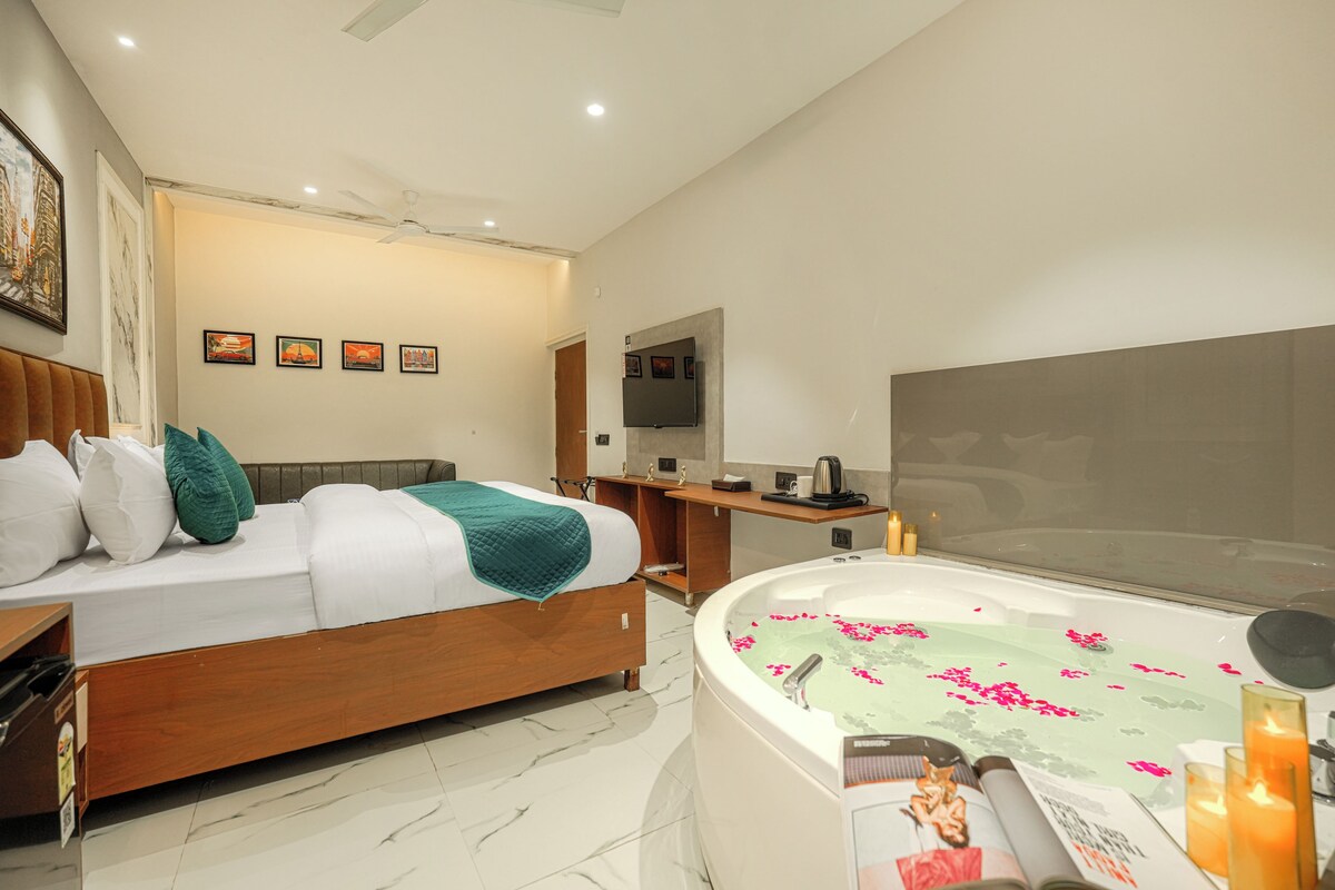 A modern hotel room with a bed, a desk, a TV, and a bathroom with a jacuzzi.