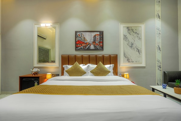 A hotel room with a bed, a nightstand, a lamp, a framed picture, and a marble wall. - THE LEAF HOTEL (Ludhiana)