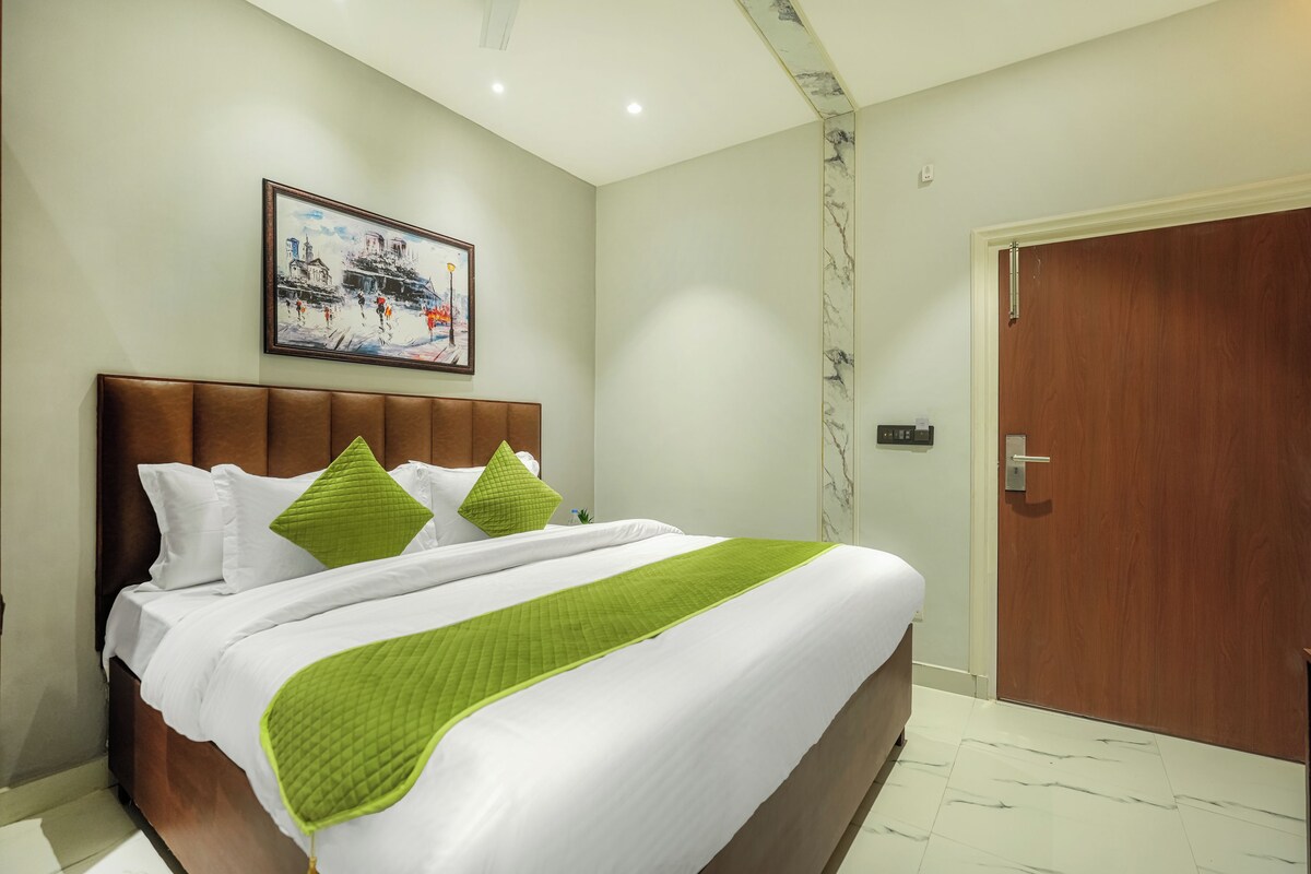 A hotel room with a bed, a painting on the wall, and a wooden door.