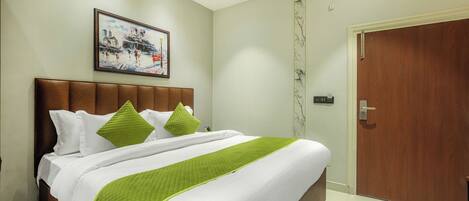 A hotel room with a bed, a painting on the wall, and a wooden door.