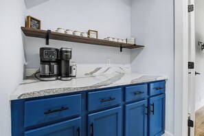 Eine Küche mit blauen Schränken, einer Kaffeemaschine und einem Regal mit Tassen.