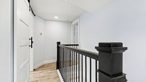 Un couloir doté d’un plancher en bois, de murs blancs et d’une rambarde noire.