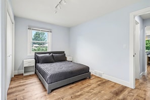 Ein Schlafzimmer mit Bett, Nachttisch, Fenster und einer Tür zu einem anderen Raum.