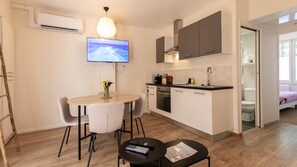 A compact kitchen with a TV, a dining area with chairs, and a small table with a remote control. - Rez-de-chaussee de la Mairie - Clim - Terrasse (Arras)