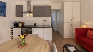 A modern kitchen with a built-in stove, a sink, and cabinets. There is a dining table with a vase of flowers. A red sofa and a lamp are visible in the living area. - Rez-de-chaussee de la Mairie - Clim - Terrasse (Arras)
