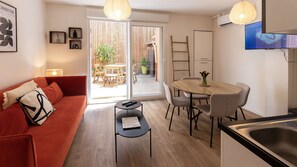 A modern living room with a red sofa, a small black table, and a dining area with a wooden table and chairs. - Rez-de-chaussee de la Mairie - Clim - Terrasse (Arras)