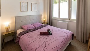 A neatly made bed with a pink and purple striped bedspread, two bedside lamps, a headboard, and a window with curtains. - Rez-de-chaussee de la Mairie - Clim - Terrasse (Arras)