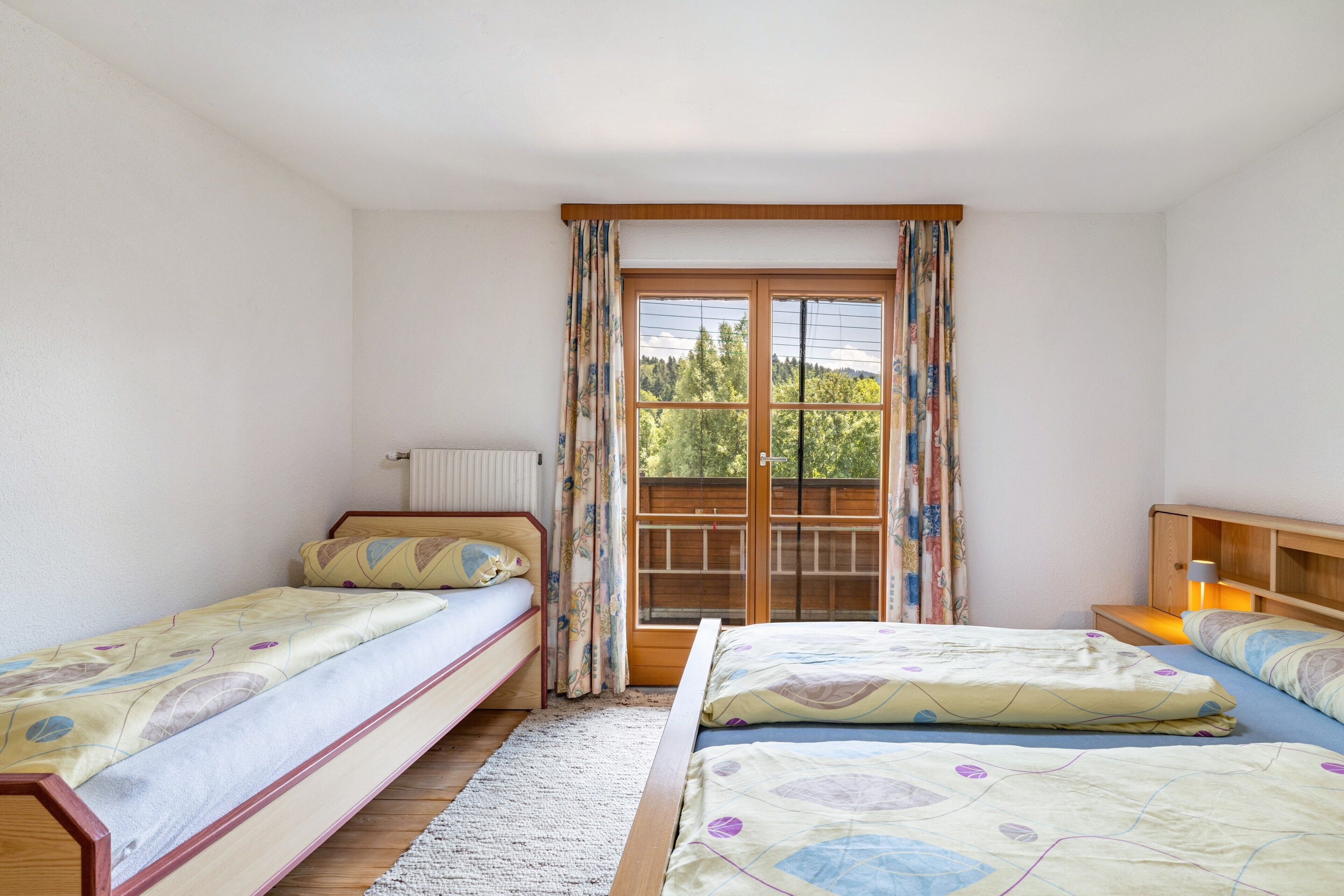 Una habitación con dos camas individuales, una ventana con cortinas, un radiador y un cabecero de madera.