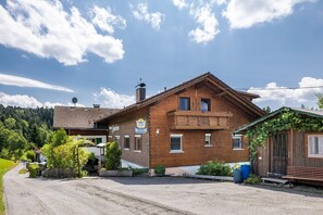 A wooden building with a balcony, a sign indicating it is a pension, and a clear sky.