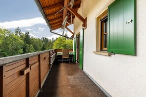 A balcony with a wooden railing, a table with a chair, and a window with green shutters.