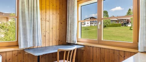 Ein Zimmer in einer Holzhütte mit Schreibtisch und Stuhl, großen Fenstern und Blick auf ein Haus und einen Rasen.