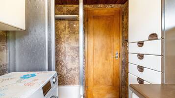 Un baño pequeño con puerta de madera, lavadora blanca y pared de azulejos.