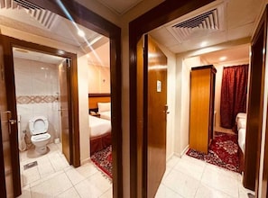 A hotel room with a bathroom, a bed, and a red carpet.