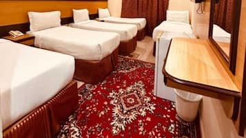 Habitación de hotel con tres camas, un escritorio pequeño, un espejo y una alfombra roja estampada.