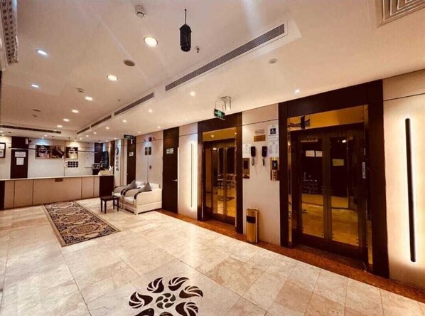 A hotel lobby with a reception desk, seating area, and a patterned floor design.