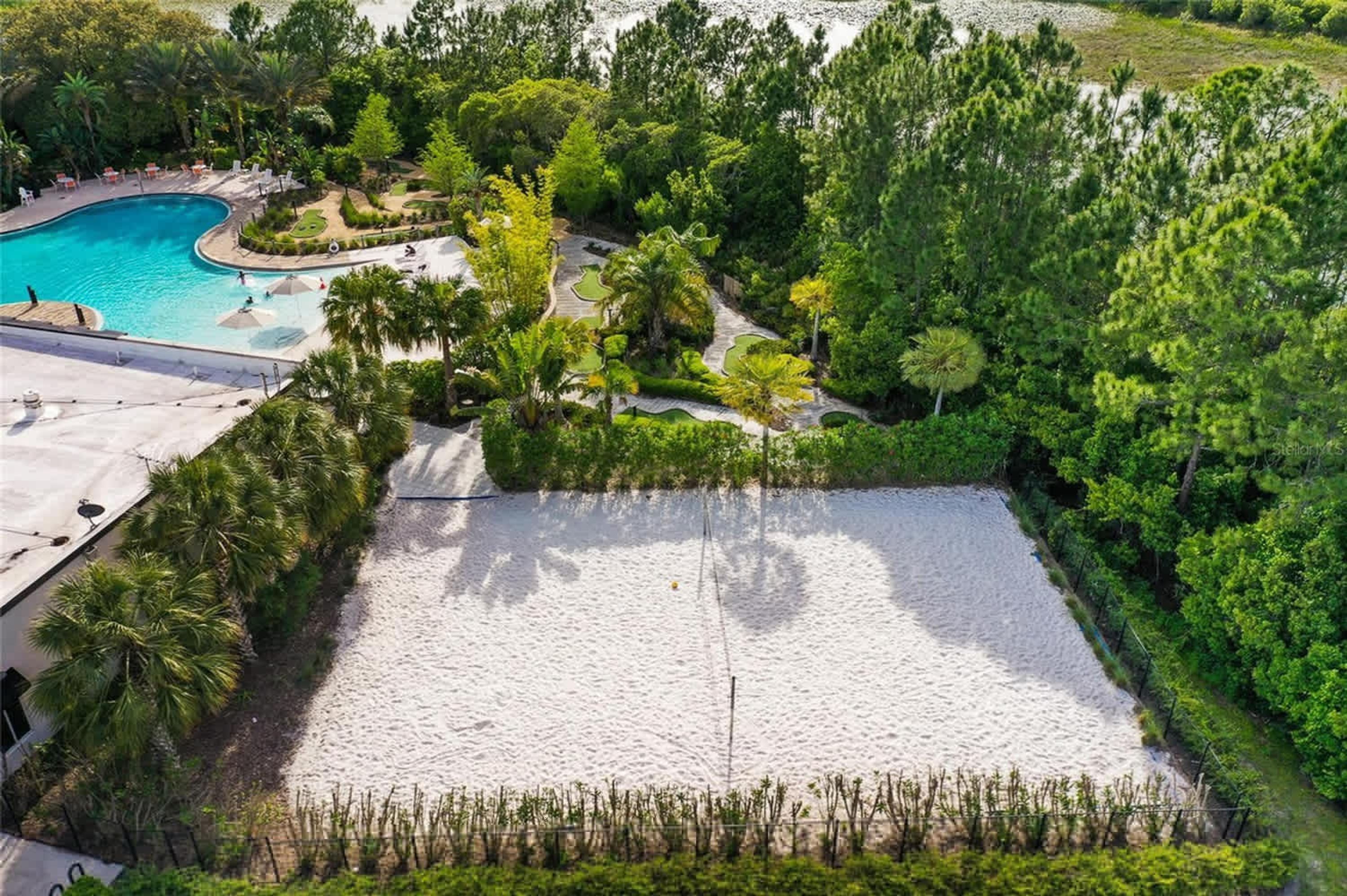 An aerial view of a resort with a swimming pool, landscaped gardens, and a sandy area.