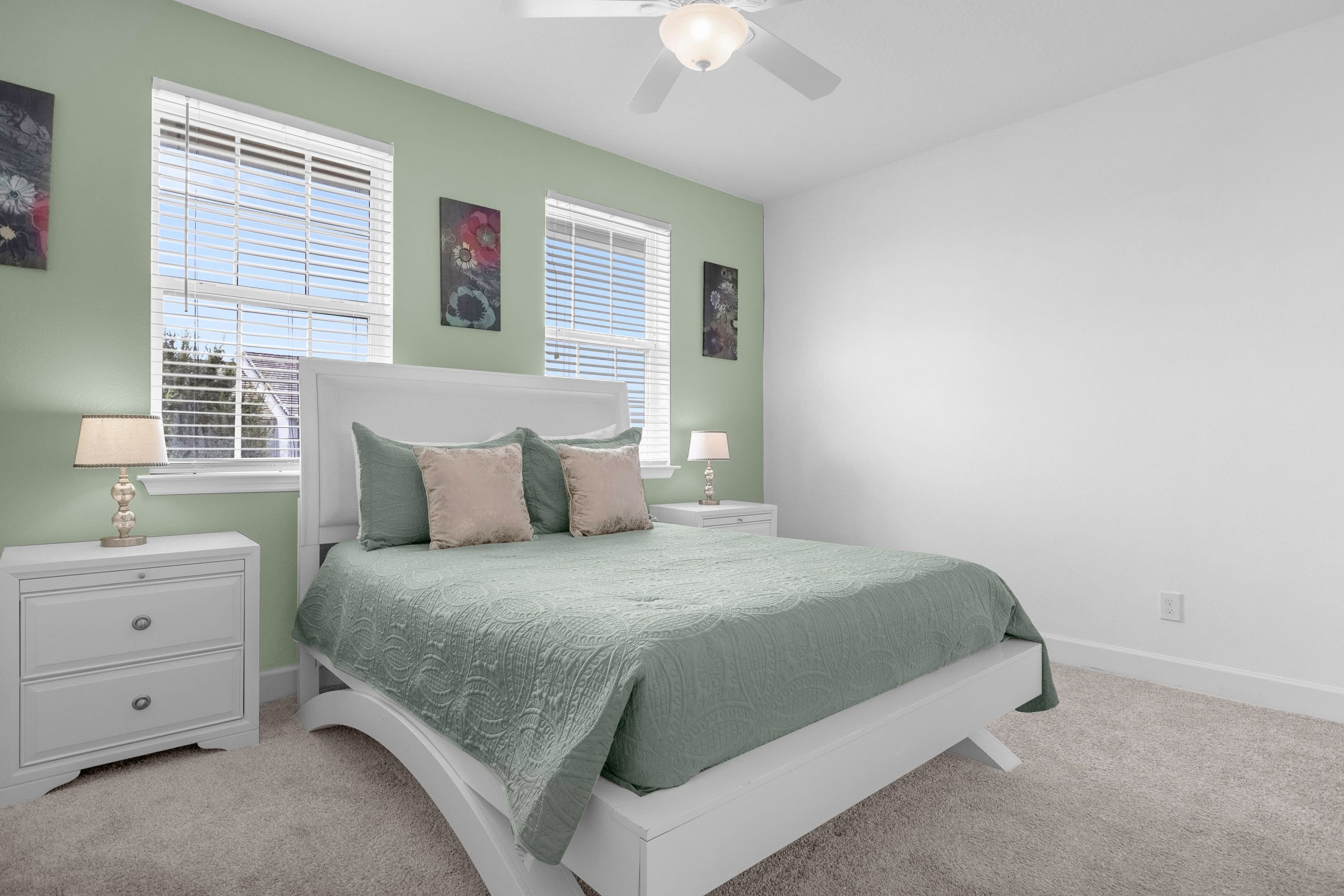 A bedroom with a bed, two nightstands, a ceiling fan, and two windows with blinds.