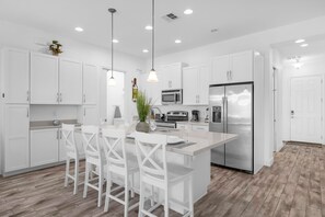 A modern kitchen with white cabinetry, a central island with bar stools, stainless steel appliances, and pendant lighting. - Upstay Family Getaway With Pool Near Disney (Davenport)