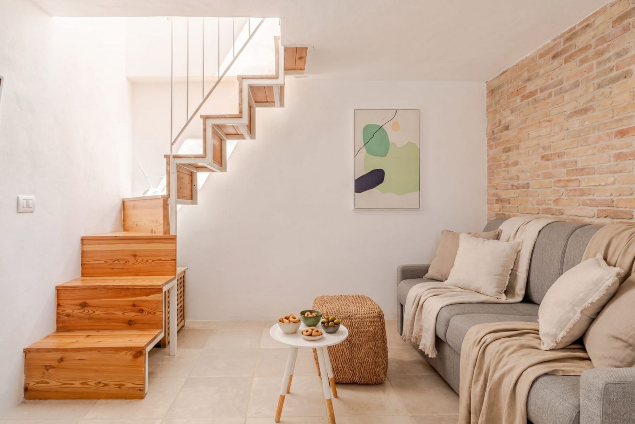Un intérieur moderne avec un escalier en bois, une table ronde sur laquelle sont disposés des bols, et un canapé gris.