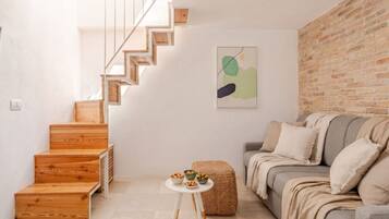 Un intérieur moderne avec un escalier en bois, une table ronde sur laquelle sont disposés des bols, et un canapé gris.