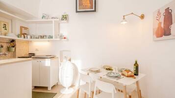 Une cuisine moderne avec des meubles blancs, une table à manger avec des chaises, un luminaire suspendu et un tableau encadré au mur.