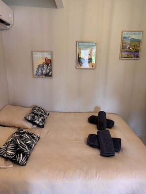 A hotel room with a bed, pillows, towels, and three framed pictures on the wall. - Studio in the Heart of Provence (Châteaurenard)