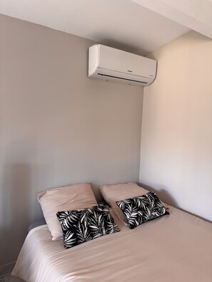 Une chambre à coucher avec un lit, deux oreillers et un climatiseur fixé au mur.