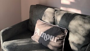 A room with a sofa, a cushion with 'Amour' text, a framed plant artwork, and a wall-mounted coat rack. - Studio in the Heart of Provence (Châteaurenard)
