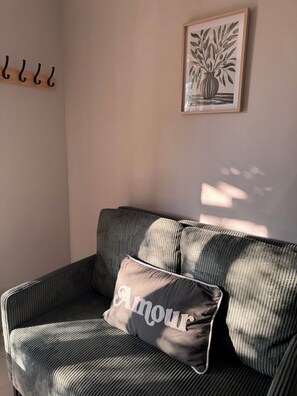 A room with a sofa, a cushion with 'Amour' text, a framed plant artwork, and a wall-mounted coat rack. - Studio in the Heart of Provence (Châteaurenard)