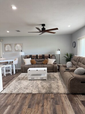 A living room with a ceiling fan, a sofa, a coffee table, a dining area with a table and chairs, and a plant. - Serenity in Seminole/Madeira Beach (Seminole)