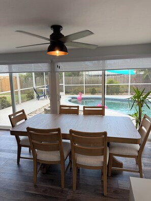 A dining area with a table and chairs, a ceiling fan, and a view of a backyard with a pool and a wooden fence. - Serenity in Seminole/Madeira Beach (Seminole)