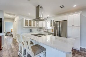 A modern kitchen with white cabinetry, a stainless steel refrigerator, and a central island with bar stools. - Serenity in Seminole/Madeira Beach (Seminole)