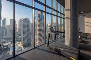 Ein Fitnessstudio mit Laufband und Trainingsgeräten, große Fenster mit Blick auf die Stadt.