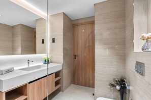 Un baño moderno con un espejo grande, lavamanos dobles, muebles de madera y una puerta de madera.