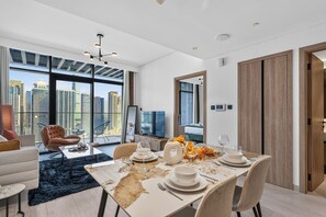 Un comedor moderno con una gran mesa dispuesta para una comida, un sofá y un televisor al fondo.