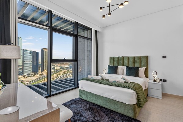 Un dormitorio moderno con un ventanal grande, una cama con ropa de cama verde, una mesita de noche y un escritorio con una lámpara.