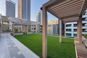 Ein Dachgarten mit Kunstgrasanlage, einer Holzpergola und modernen Gebäuden im Hintergrund.