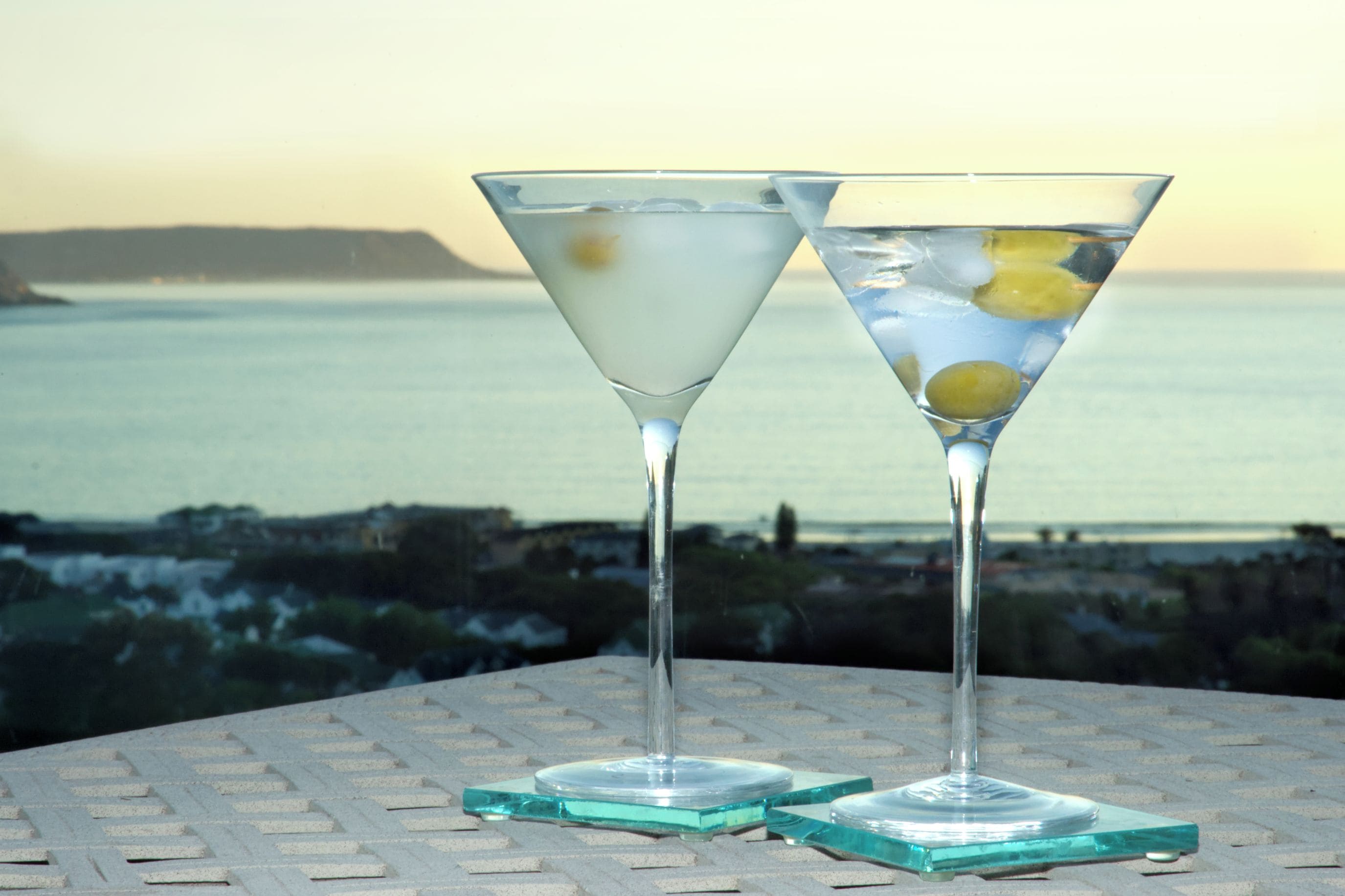Two martini glasses with a coastal view in the background.
