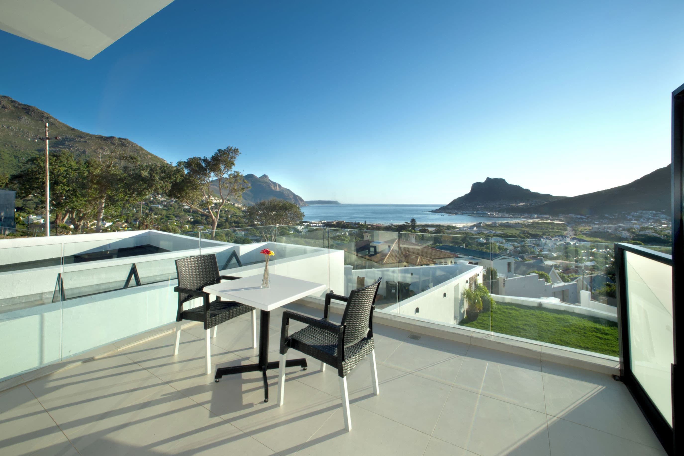 Une terrasse avec une table et des chaises, offrant une vue sur un paysage côtier avec des montagnes et la mer.