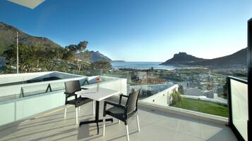 Une terrasse avec une table et des chaises, offrant une vue sur un paysage côtier avec des montagnes et la mer.