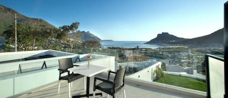 A terrace with a table and chairs, overlooking a coastal landscape with mountains and a view of the sea.