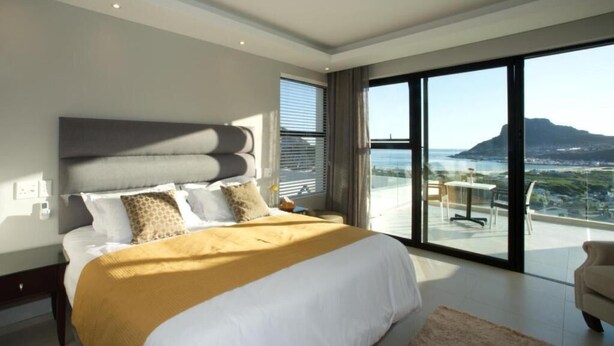 A modern bedroom with a large bed, a view of the ocean, and a balcony.