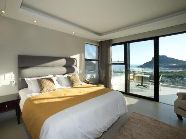 A modern bedroom with a large bed, a view of the ocean, and a balcony.