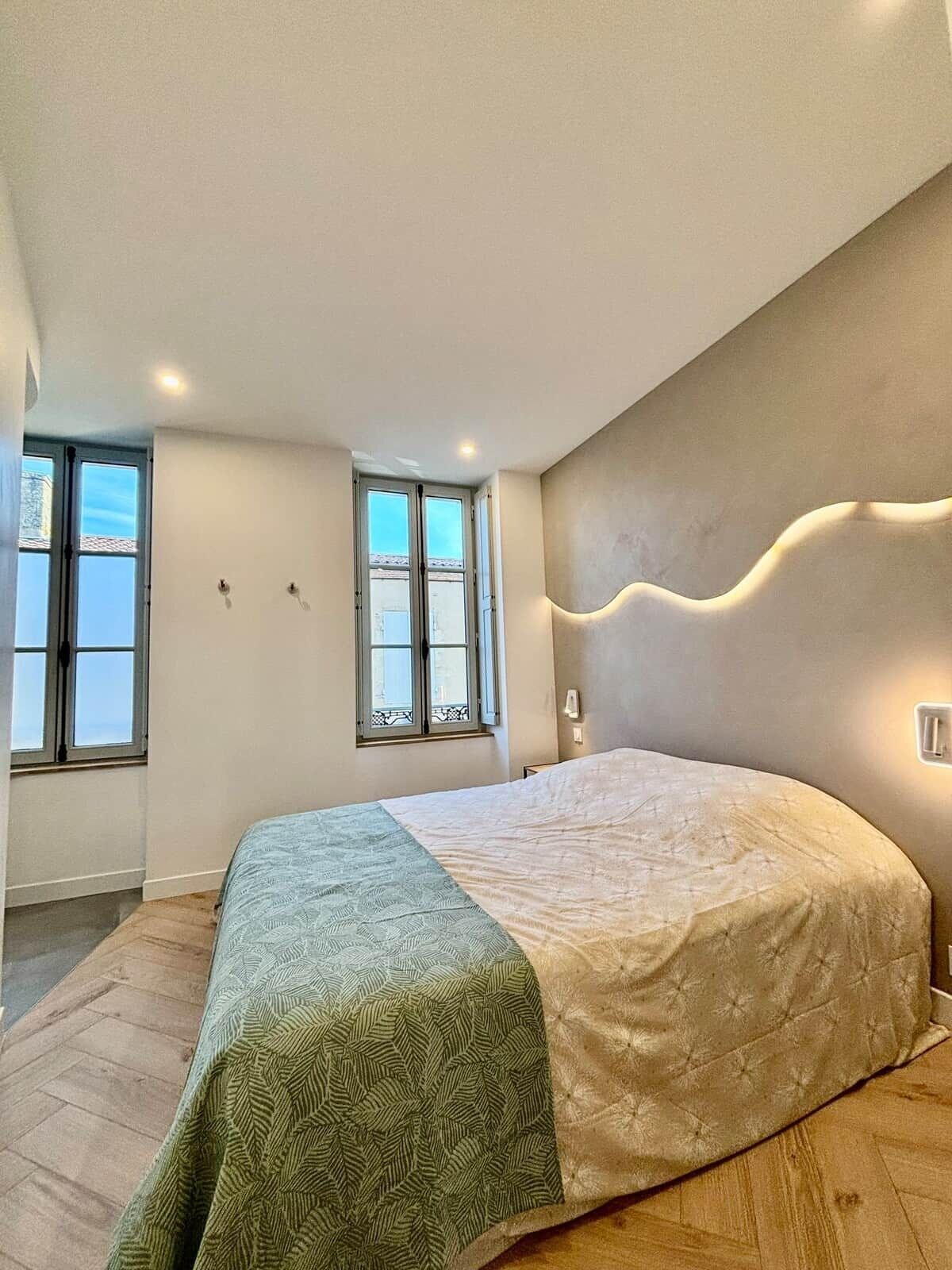 Une chambre à coucher avec un lit, deux fenêtres, un luminaire et une lampe fixée au mur.