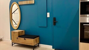A room with a blue accent wall, a wooden cabinet with a black seat, a round mirror, a door with a handle, and a built-in oven.