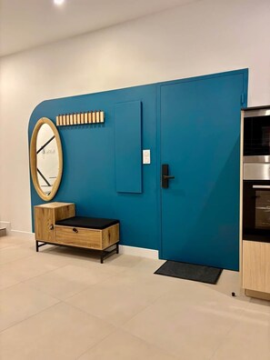 A room with a blue accent wall, a wooden cabinet with a black seat, a round mirror, a door with a handle, and a built-in oven. - Luxury Triplex • Garden • Freestanding Bathtub • Citadel (Blaye)