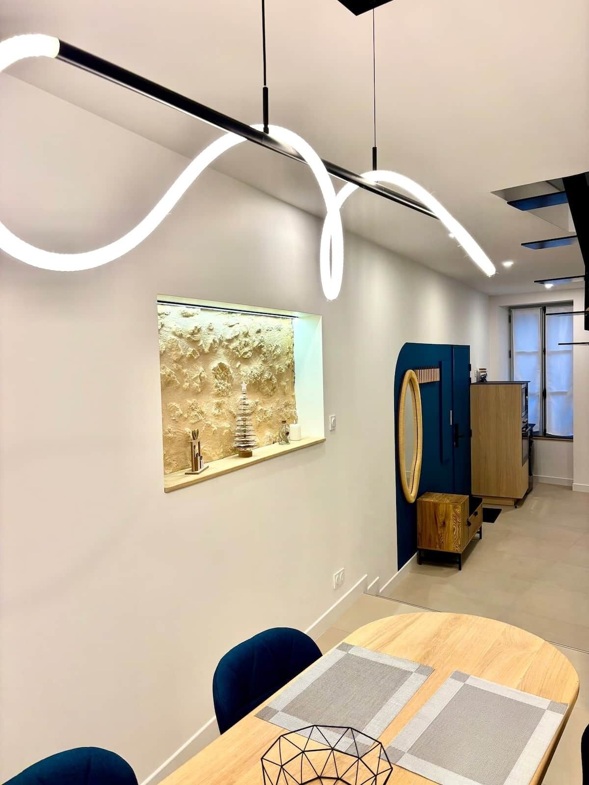 Um interior moderno com uma mesa de jantar de madeira, cadeiras azuis, uma obra de arte geométrica na parede e um detalhe de parede com textura única.