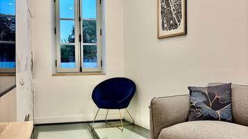 Een moderne woonkamer met een glazen tafel, een blauwe stoel, een grijze bank en een lijstwerk op de muur.