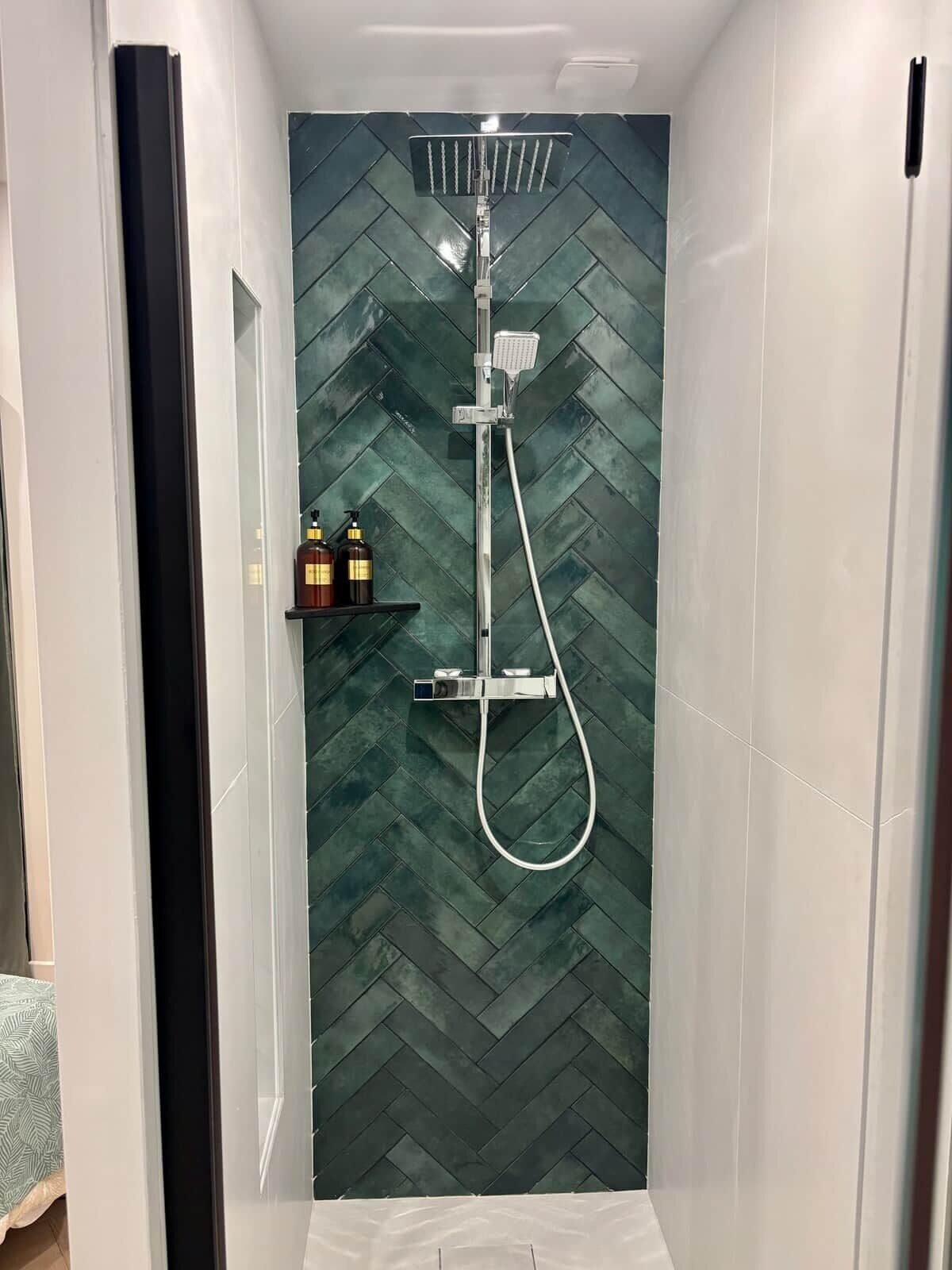 A shower with a herringbone tile pattern, a handheld showerhead, and a handheld shower attachment.